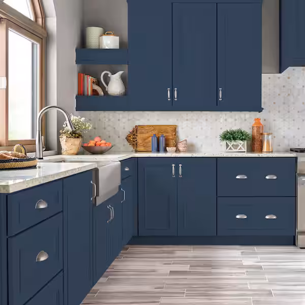 Blue paint colors for kitchen cabinets: Modern L-shaped kitchen featuring navy blue cabinets with silver hardware, white marble-look countertops, hexagonal backsplash, and a farmhouse sink. Gray wood-look flooring and open shelving complete the contemporary design